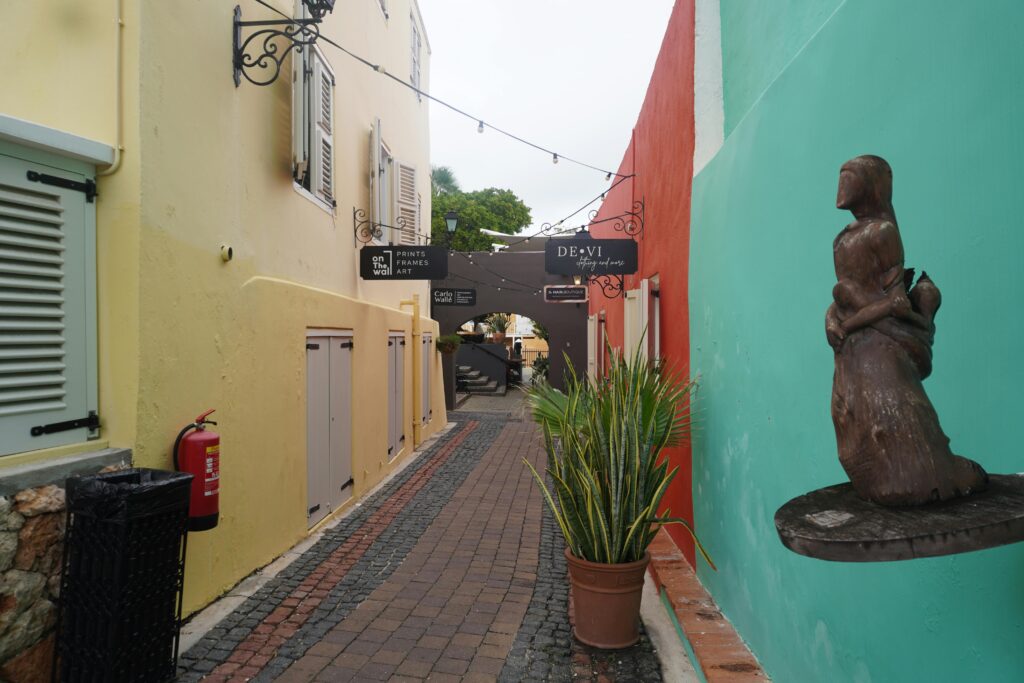 Charming alley in Willemstad, Curaçao featuring colorful walls and street art sculpture.